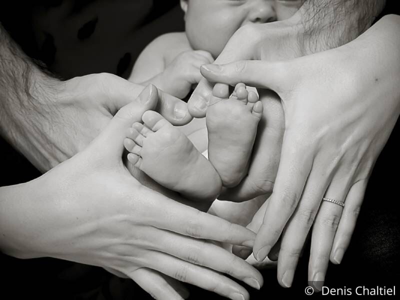 Photo en noir et blanc de parents tenant leurs mains en forme de coeur autour des pieds de leur bébé.